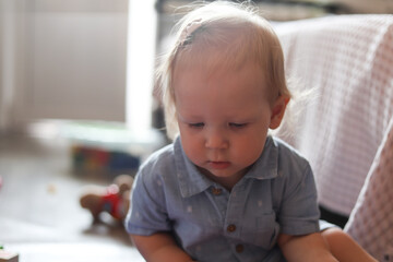 Fototapeta premium Young child with blonde hair looking down thoughtfully indoors