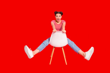 Fototapeta premium Nice-looking attractive glamorous lovely shine crazy girl wearing striped tshirt jeans sitting on chair having fun fooling isolated over pink pastel background