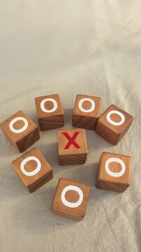 Players use wooden blocks to play tic tac toe on a table at home. One player marks an X while the other uses O. The game unfolds with each round.