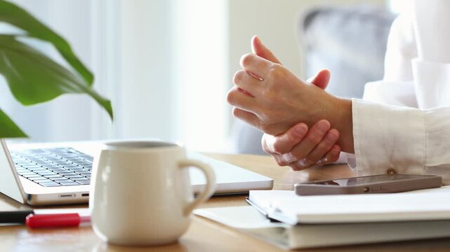 Young woman massaging aching wrist and fingers on hands after laptop typing, showing pain, arthritis and carpal tunnel syndrome at home remote workplace.