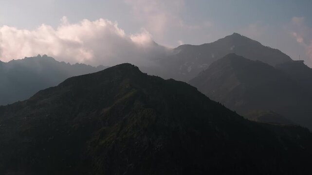 Aerial view of a dark, moody mountain silhouette beneath heavy storm clouds, capturing a brooding dusk atmosphere over the alpine landscape.
