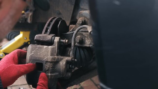 Dislodging seized caliper guide pin with screwdriver and impact force during vehicle maintenance procedure. Automotive repair concept with rusted component extraction, closeup mechanical disassembly