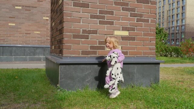 Little girl playing with toy dog near brick pillar in courtyard