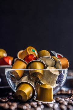 Assorted Coffee Capsules in Glass Bowl with Coffee Beans on Dark Background