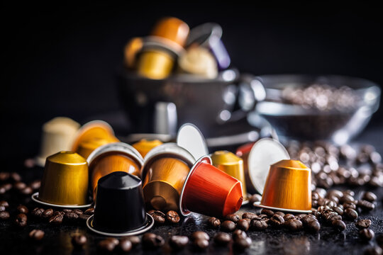 Colorful Coffee Capsules and Espresso Pods Scattered Among Roast Coffee Beans on Dark Surface