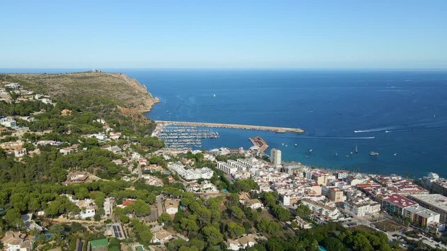 Javea port and residential area with mediterranean sea, beach, and cabo de san antonio under clear blue sky.