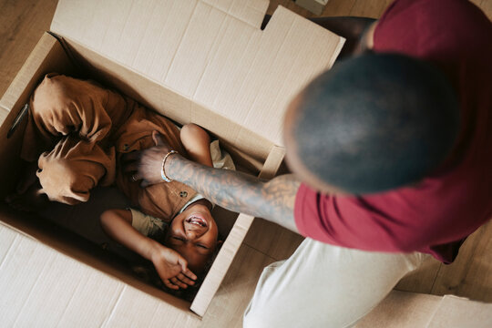 Directly above shot of man tickling his son hiding inside moving box