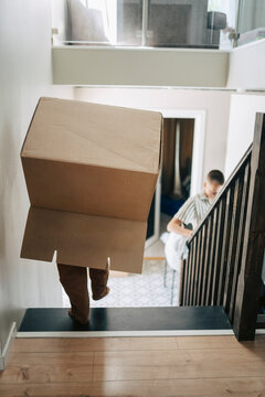 Boy hiding under moving box while moving down on stairs at home