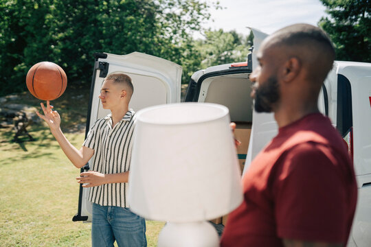Boy spinning basketball on his finger while standing next to van during house move