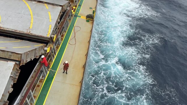 crew wash ship cargo hold coaming during sea passage.