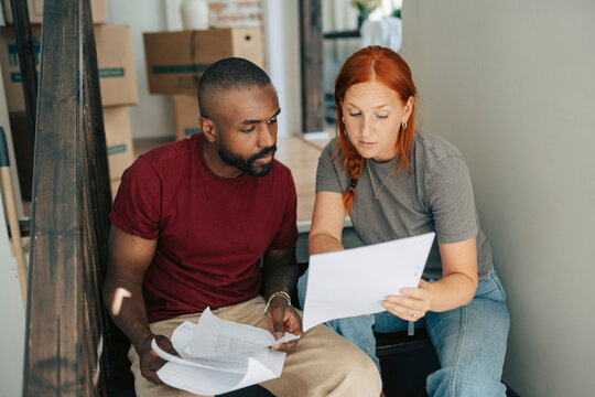 Redhead woman explaining house layout to man while sitting on staircase