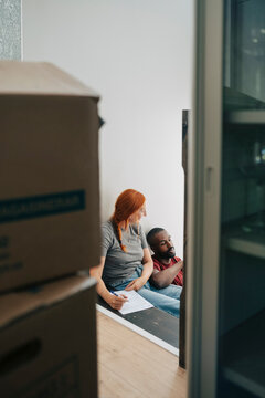 Diverse couple sitting on stairs with moving boxes in new home