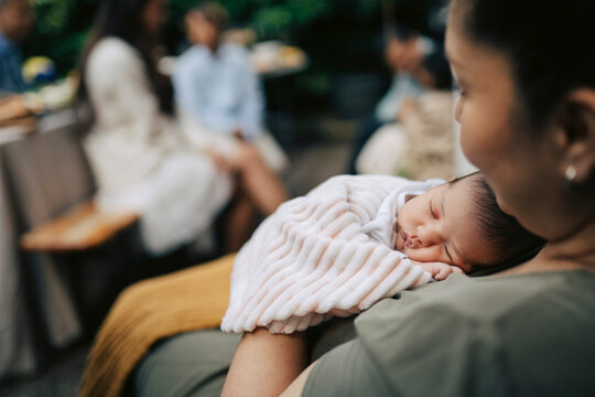 Sleeping newborn baby resting on mother's shoulder at family gathering