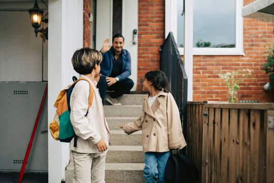 Children waving goodbye to their father while leaving for school