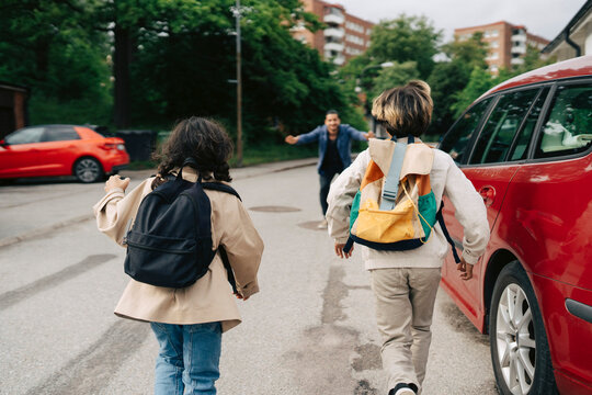 Son and daughter with backpacks running toward their father standing on road