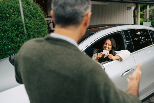 Smiling girl showing her driving license to father while sitting in car