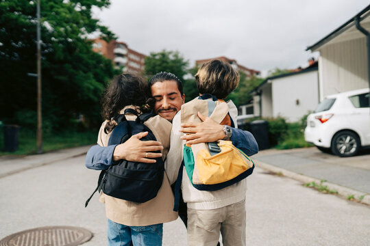 Smiling man embracing his son and daughter after first day of school