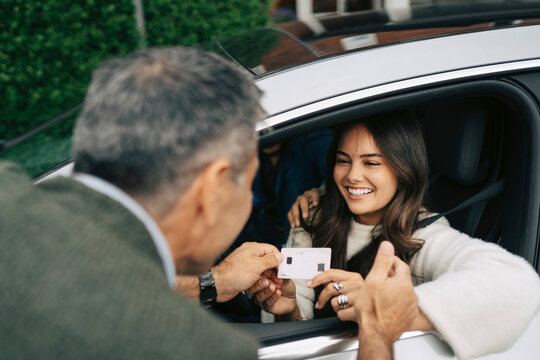 Smiling woman showing new driving license to her father while sitting in car