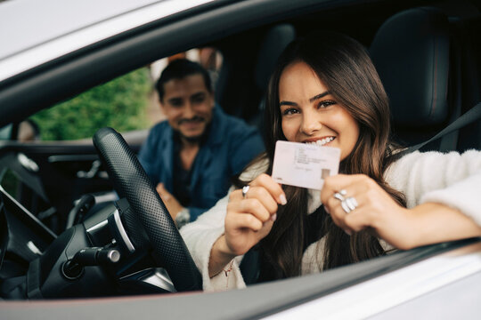 Portrait of smiling young woman showing her driving license while sitting in car