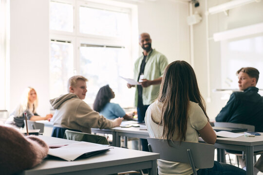 Rear view of teenage girl with long hair sitting at desk in classroom