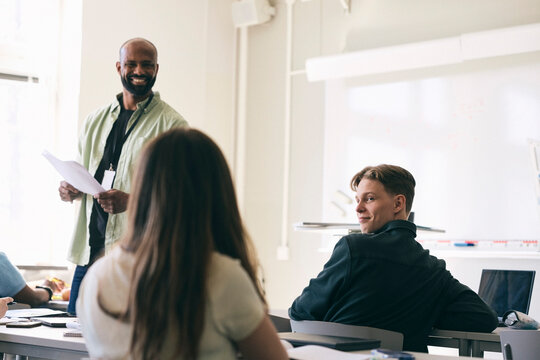 Smiling teenage boy looking over shoulder at female classmate while sitting in school
