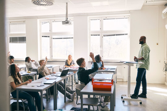 Teenage students raising hands during Q and A session in classroom at high school