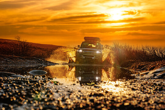 Off Road SUV Splashing Through Mud at Sunset.