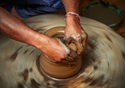 Skilled artisan hands shaping wet clay on a spinning potter wheel, creating a ceramic vase in a traditional pottery workshop.