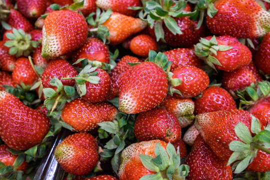 Fresh ripe strawberries with green leaves forming a colorful natural fruit background.