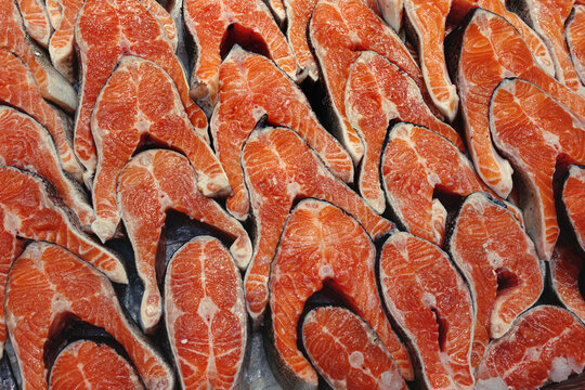 Fresh raw salmon steaks on display, bright orange fish meat with marble texture and skin, ready for cooking, seafood market background.