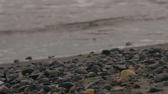 Low-angle view of many small stones on a beige sandy beach with gentle waves quietly washing ashore in the background