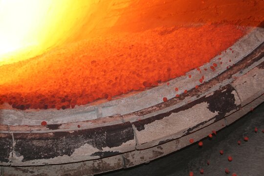 Industrial hot pyrometallurgical rotary kiln discharging red hot ore pellets. High temperature roasting, oxidation, reduction chemical reaction. Metallurgical mining processing mill. Copy space