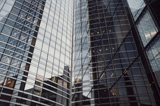 Reflective glass architecture with office windows and geometric facade patterns rises through a tight upward view of modern towers in a dense business setting