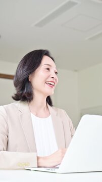スーツを着て笑顔で顧客と対面相談する50代女性、オフィスで説明や提案を行うビジネスウーマン　コミュニケーションや商談などのビジネスイメージの縦動画
