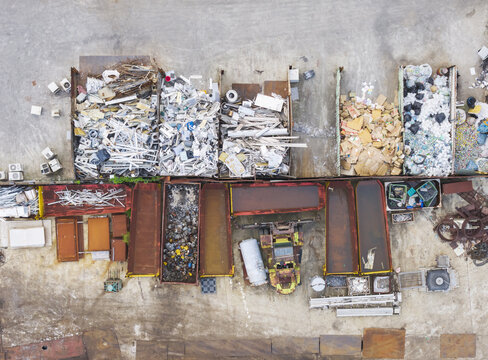 Aerial view of a recycling plant with various sorted waste materials in containers, including scrap metal, cardboard, and plastics, arranged in an industrial yard in Taiwan.