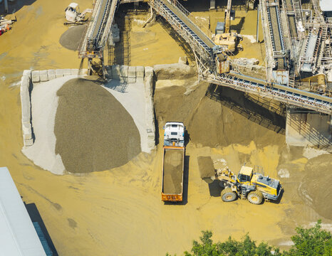 Aerial view of a construction aggregate plant with conveyor belts, piles of gravel, and a yellow front-end loader filling a dump truck in Taiwan.