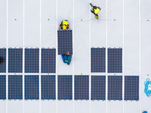 Aerial view of workers in high-visibility vests installing solar panels on a floating marine fish farming pen in Liabygda, More og Romsdal, Norway.