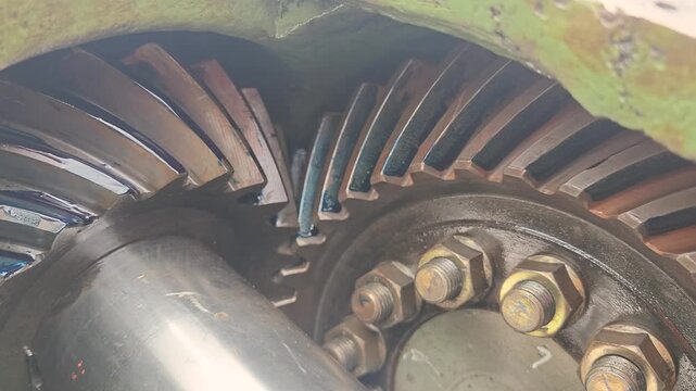 Heavy-duty spiral bevel gear assembly meshing together, featuring detailed teeth contact patterns with blue lubrication dye on the mechanical component. Industrial machine equipment part, close-up wit