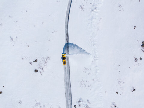 Aerial view of a yellow snowblower clearing a snow-covered road through a vast white winter landscape in Valldal, More og Romsdal, Norway.
