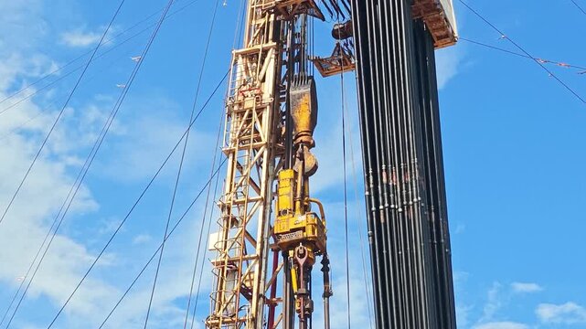 Drilling rig with top drive system (TDS) during tripping in the drill pipe to drill the hole in crude oil exploration operation with sunny blue sky background. Heavy industrial working scene.