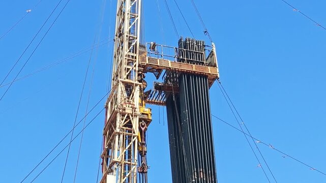 Drilling rig with top drive system (TDS) during tripping in the drill pipe to drill the hole in crude oil exploration operation with sunny blue sky background. Heavy industrial working scene.