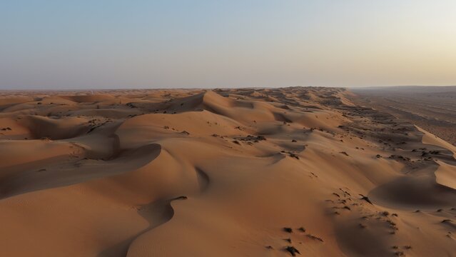Aerial view of the vast undulating sand dunes of Wahiba Sands desert under a clear sky in Muscat, Muscat Governorate, Oman.