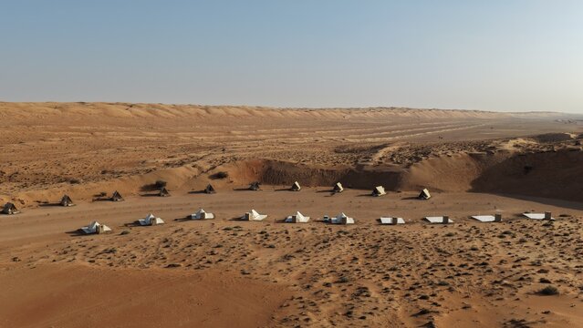 Aerial view of a desert camp with white tents arranged in the sandy landscape of the Wahiba Sands near Muscat, Muscat Governorate, Oman.