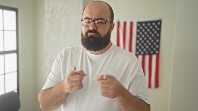 Man points fingers at camera in studio with american flag and white t shirt; patriotism civic duty serious.