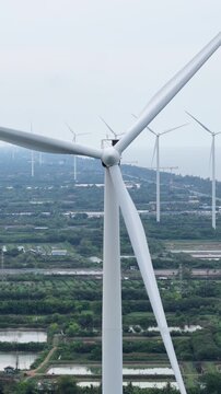 A vertical aerial view of numerous wind turbines for electricity generation near the sea with shrimp ponds and farmland below.
