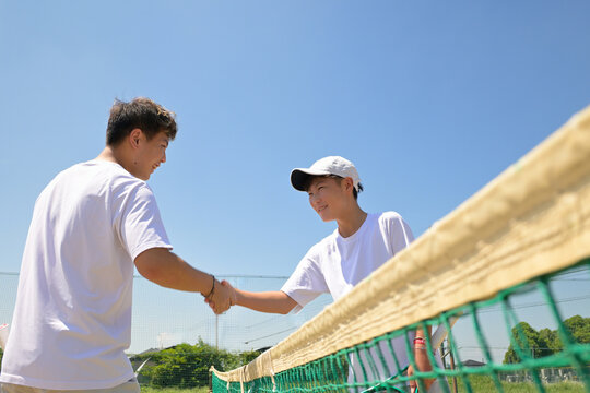 テニスの試合前にネットを挟んでエガをで握手をする二人の男子選手