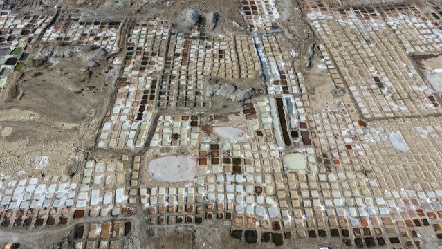 Aerial view of the salt pans in Qurayyat, featuring a grid of evaporation ponds with varying water colors and textures in Qurayyat, Muscat Governorate, Oman.