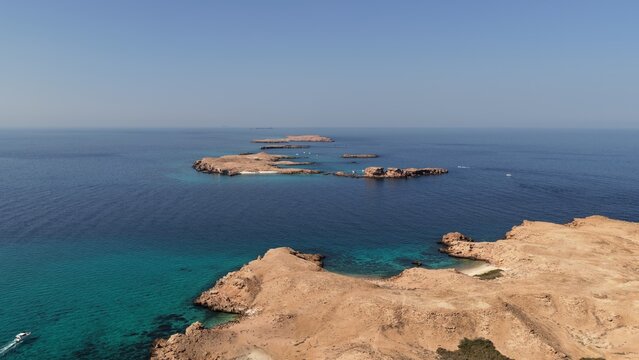 Aerial view of Daymaniat Islands featuring turquoise waters, rocky coastline, and a small boat navigating the sea, Sib, Oman.