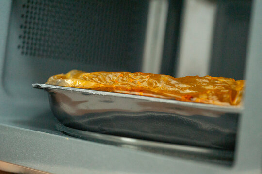 baking dish with lasagna or pie inside an open microwave oven or mini oven kitchen appliance concept of food preparation cooking