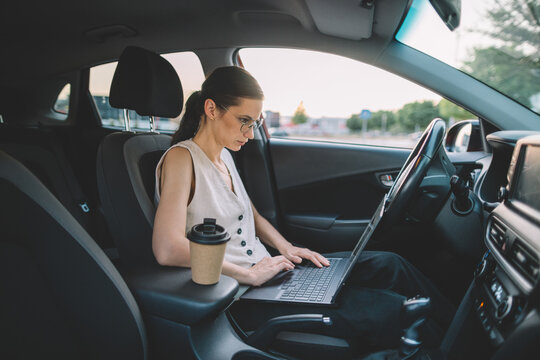 Businesswoman working on a laptop while sitting in a parked car